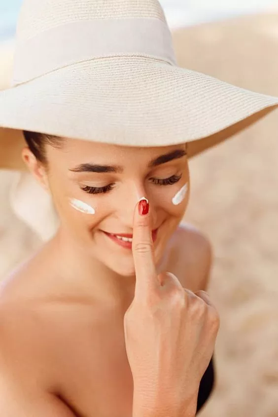 mulher com a mão no nariz passando protetor solar para cuidar com a pele no verão