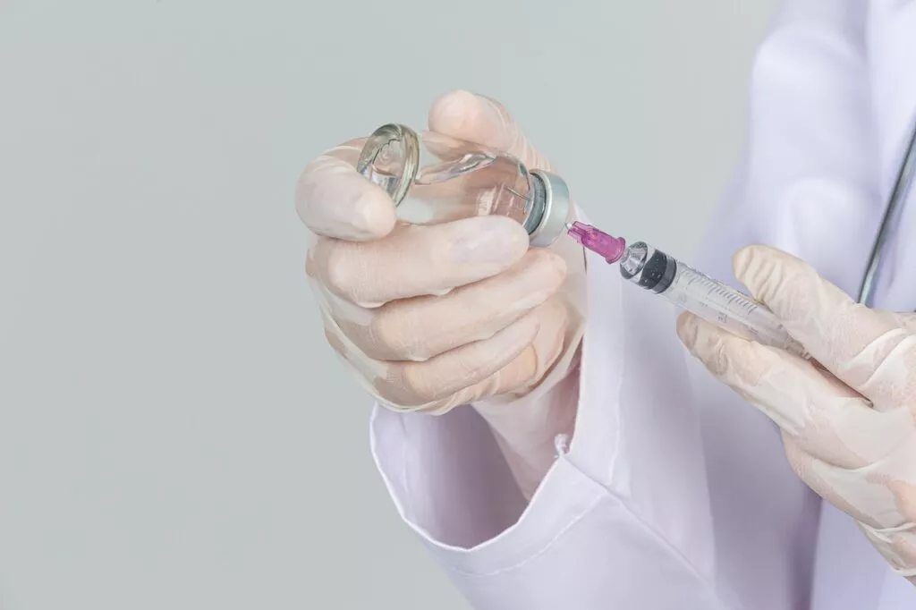 young doctor is holding hypodermic syringe with vaccine vial rubber gloves gray wall