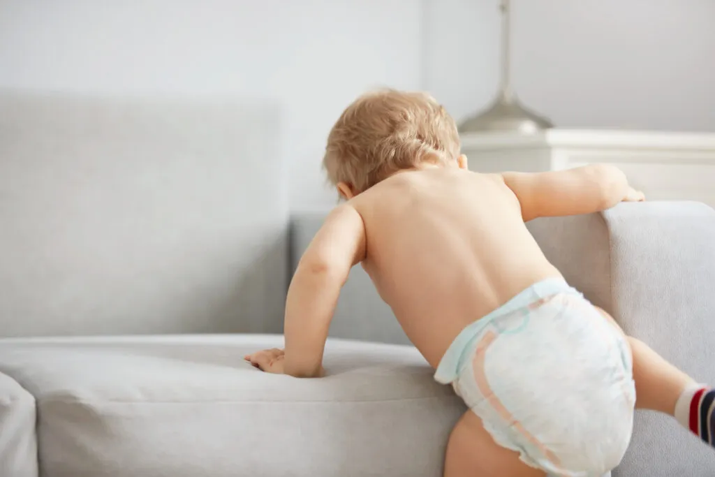 Bebê subindo na cama, mostrando sua curiosidade e energia infantil, em um ambiente doméstico aconchegante.